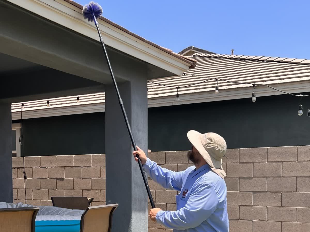 Peterson Pest Management technician de-webbing the eaves of an East Valley home with an extension duster